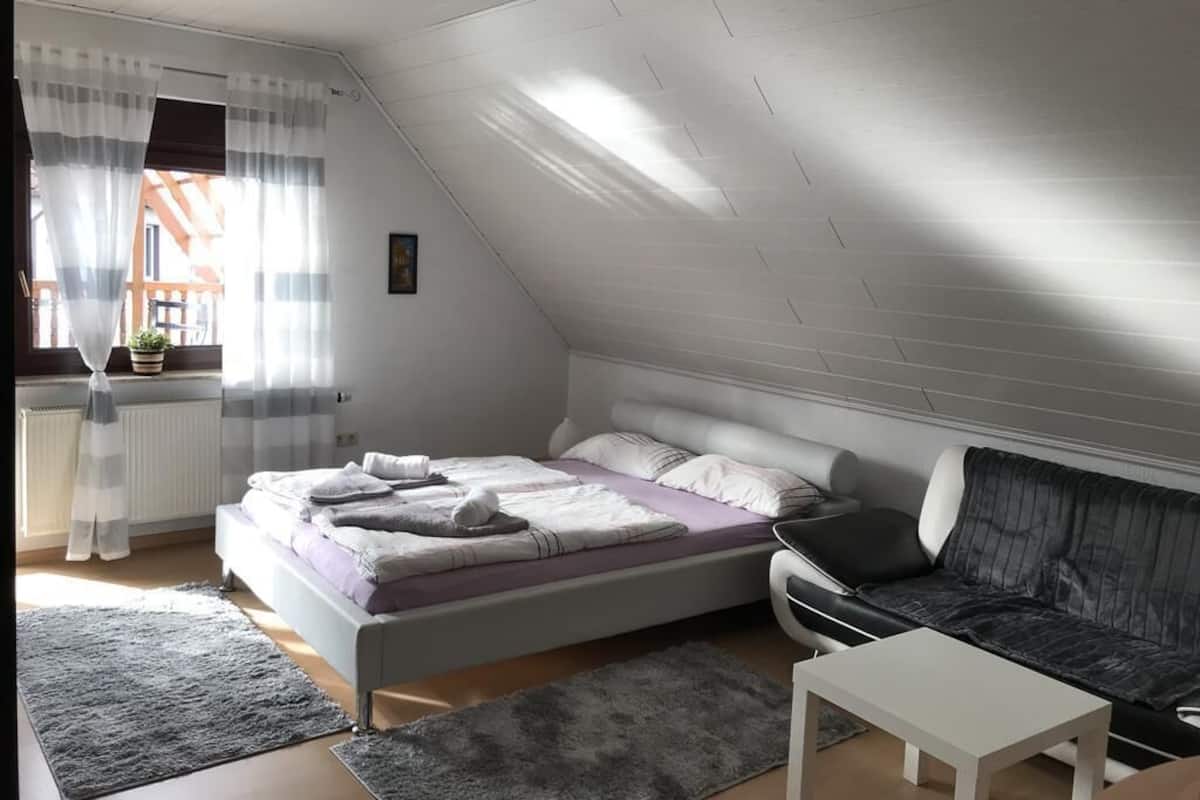 Une chambre à coucher avec un lit, un canapé, une petite table et une fenêtre avec des rideaux.