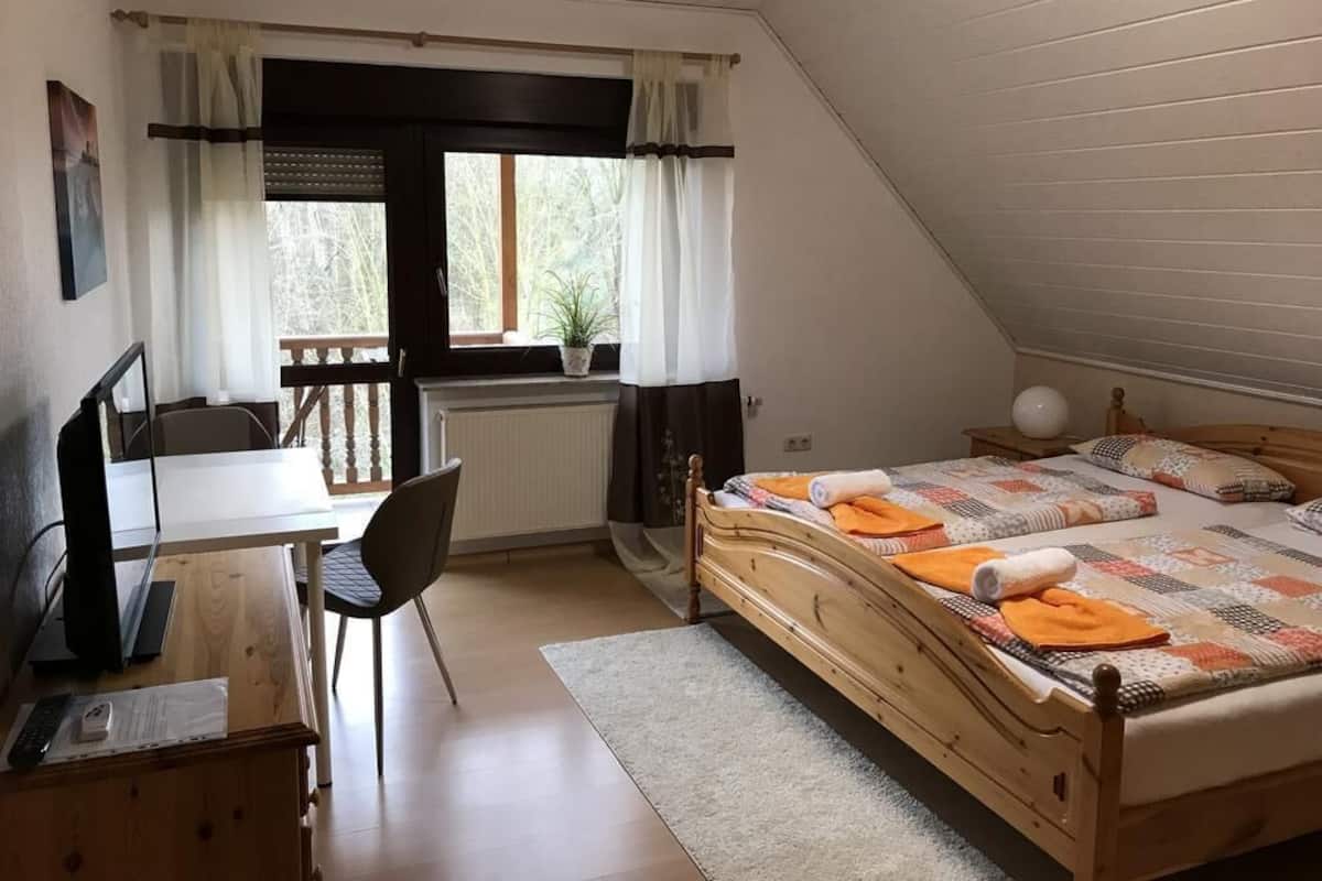Une chambre à coucher avec un lit en bois, un bureau avec une chaise, un radiateur et une fenêtre avec des rideaux.