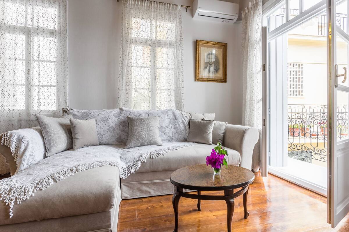Una sala de estar con un sofá seccional color beige, una mesa de centro redonda de madera y vistas a un balcón con barandilla de hierro forjado.