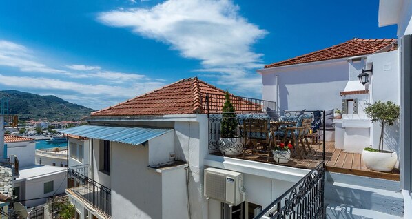 A residential building with a red-tiled roof, white walls, and a balcony with outdoor furniture.