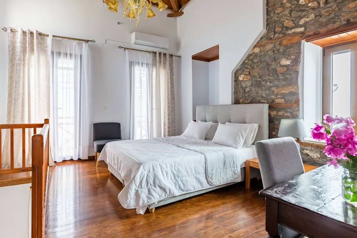 Un dormitorio con una cama grande, una silla, un escritorio y una pared de piedra.