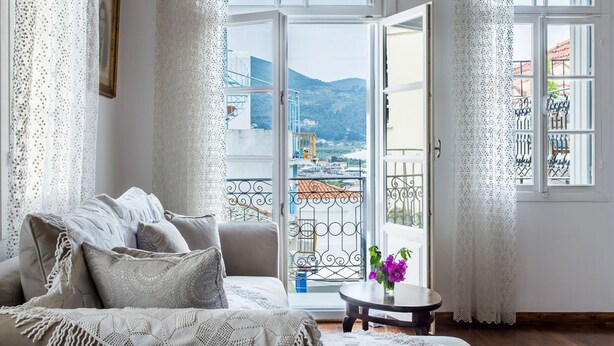 Una sala de estar acogedora con un sofá, una mesita con un florero y un balcón con vistas a la ciudad y las montañas.
