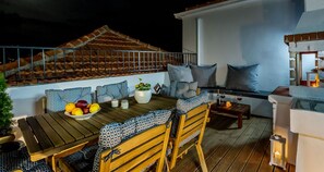 A wooden deck with a table set for dining, surrounded by patterned cushions and a potted plant.