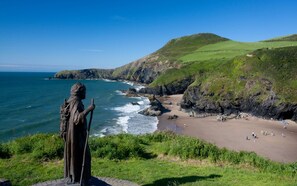 A coastal view with a statue overlooking a beach and cliffs. - Parc-yr-Hebog (Lampeter)
