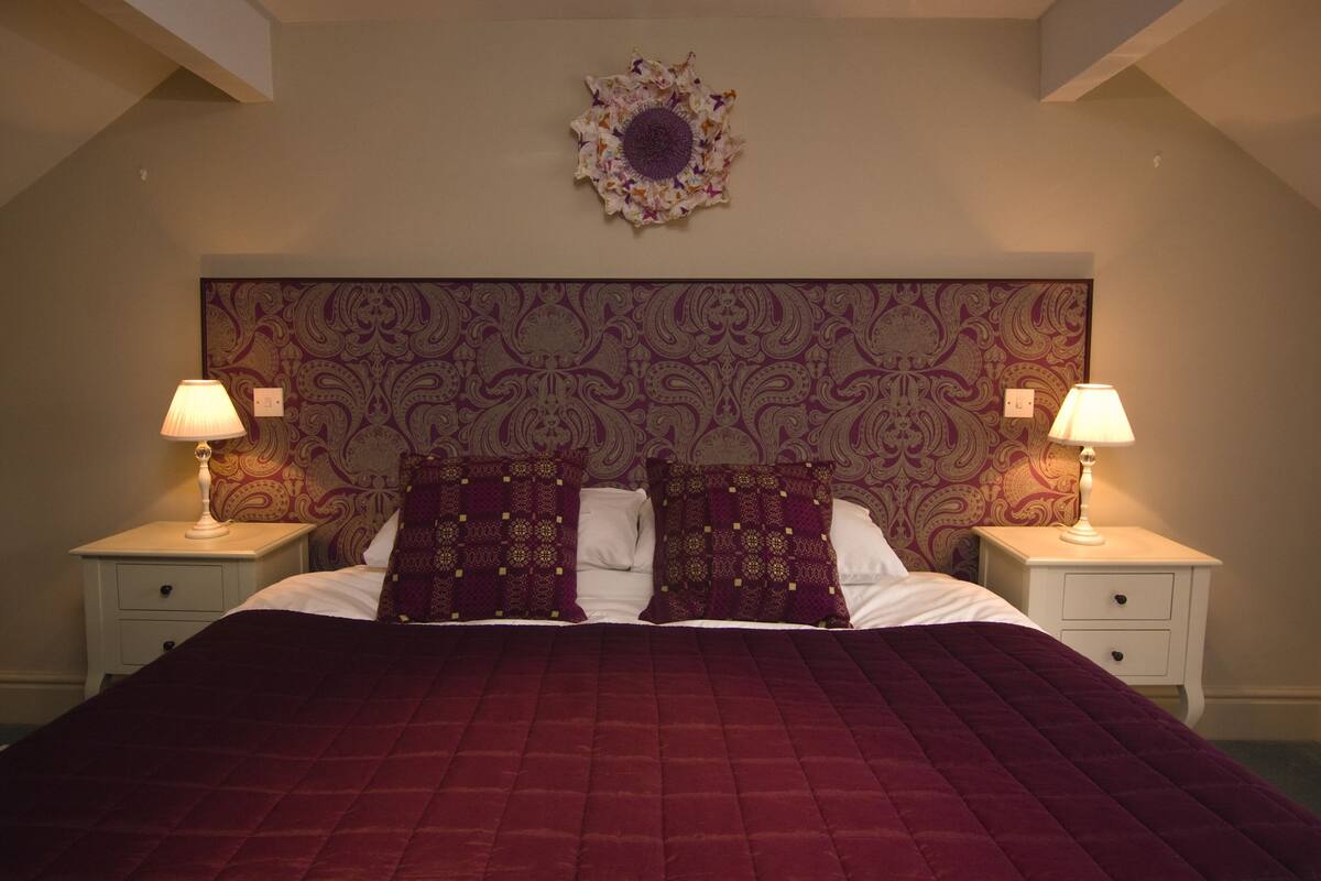 A bedroom with a large bed, two bedside tables with lamps, and a decorative wall hanging above the bed.