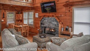 A cabin interior with a stone fireplace, wooden furniture, and a mounted television. - Chasing Rainbows (Mineral Bluff)