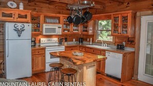 A cabin kitchen with wooden cabinets, a central island, a refrigerator, a microwave, and a sink. - Chasing Rainbows (Mineral Bluff)