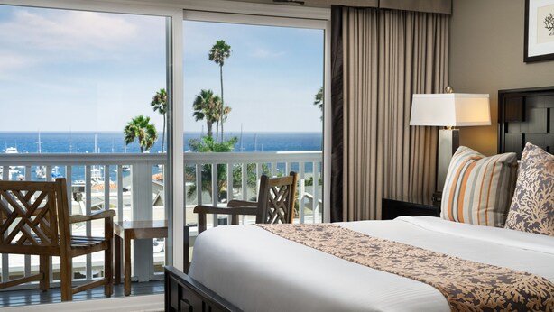 Ein Hotelzimmer mit Balkon und Meerblick, ein Bett mit gemustertem Überwurf sowie ein Nachttisch mit Lampe.