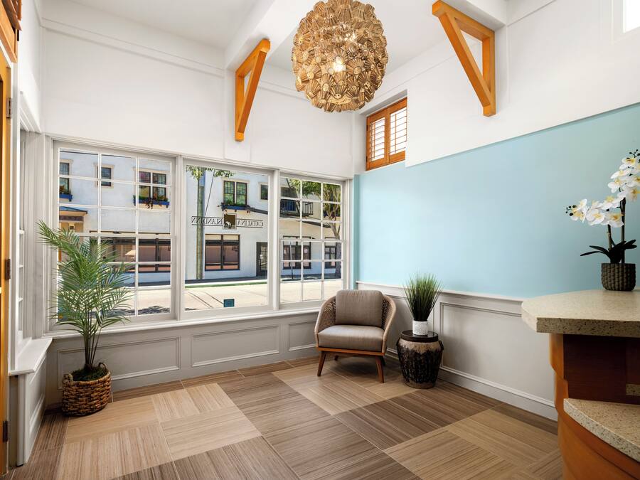 A room with large windows, a chair, a potted plant, and a unique chandelier.