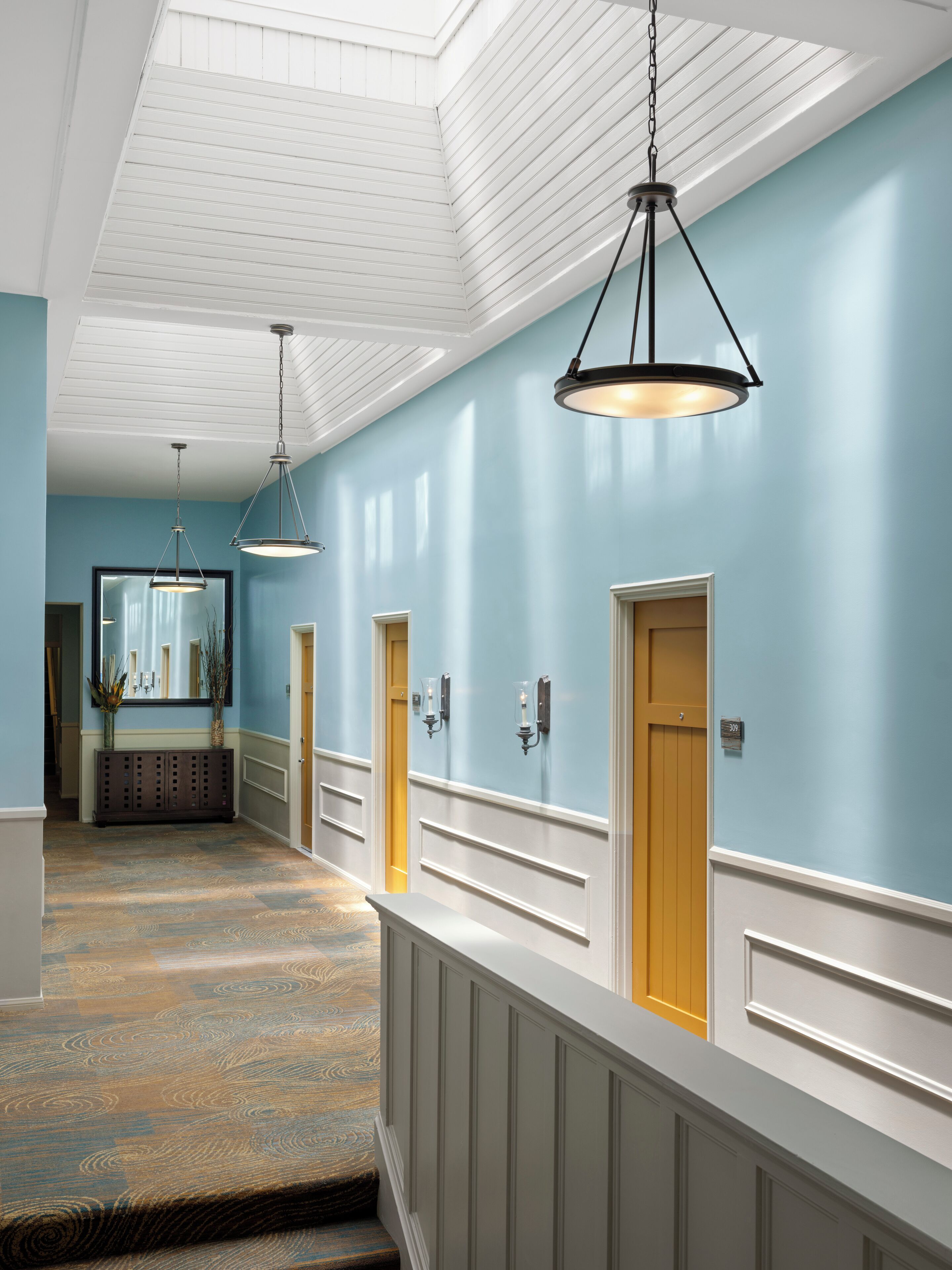 A hallway with a blue wall, wooden doors, and a white railing.