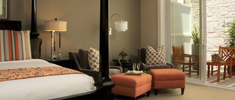 A hotel room with a four-poster bed, two ottomans, a sofa, a chair, a small table with a tray, and a potted plant.