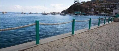A sandy beach with a rope barrier and a view of boats on the water.