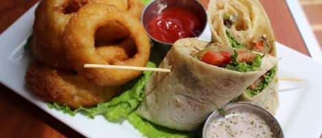 A plate with onion rings, a wrap, and two dipping sauces.