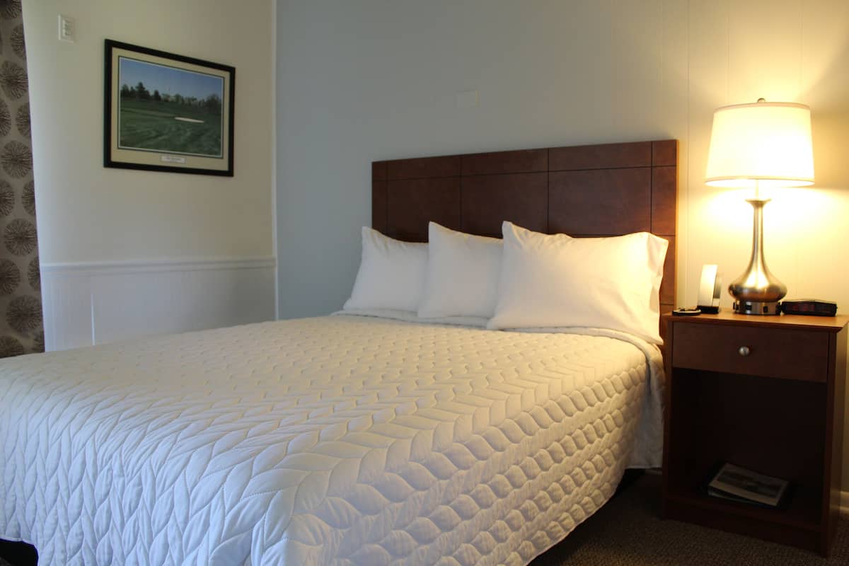A neatly made bed with a quilted white bedspread, a wooden headboard, and a bedside table with a lamp and a book.