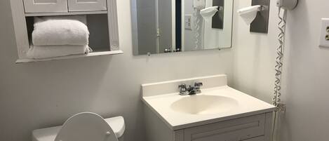 Une salle de bain avec un lavabo blanc, des toilettes, un porte-serviettes, un miroir et un sèche-cheveux.