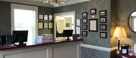 A reception area with a desk, computer, printer, framed certificates, and a chandelier.