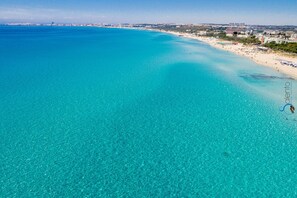 An aerial view of a coastal area with clear turquoise waters, a sandy beach, and a cityscape in the background. - Villa Carriero (Gallipoli)