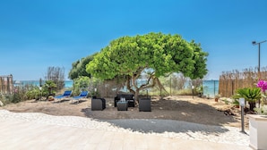 Un espace extérieur aménagé en terrasse, avec des sièges, un arbre et une vue sur la mer.