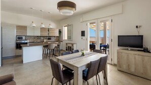 Une cuisine moderne dotée d’un îlot central, d’un coin repas avec des chaises et d’un téléviseur posé sur un meuble.