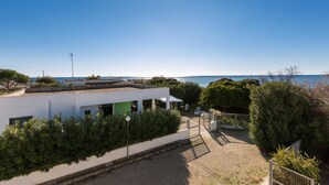 Un bâtiment moderne doté d’un patio couvert, d’une cour sablonneuse et d’une vue sur la mer.