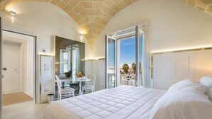 A bedroom with a large bed, a desk, and a chair, a bathroom with a shower, and a balcony with a view. - Acquaviva Suites (Diso)