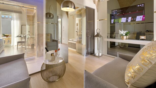 A modern living room with a sofa, a round coffee table, and a TV displaying a guide channel. - Acquaviva Suites (Diso)