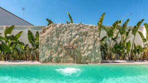 A swimming pool with clear turquoise water, surrounded by lush tropical plants and a large rock feature. - Acquaviva Suites (Diso)