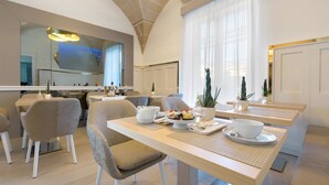 A modern dining area with a high ceiling, large windows, and a kitchen in the background. - Acquaviva Suites (Diso)