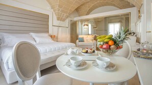 A hotel room with a bed, a dining table with a fruit bowl, and a mirror. - Acquaviva Suites (Diso)