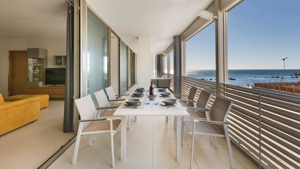 A modern dining area with a table set for six, large windows offering a view of the sea, and a yellow sofa in the background. - 1327 Appartamento Spinalonga by Barbarhouse (Gallipoli)