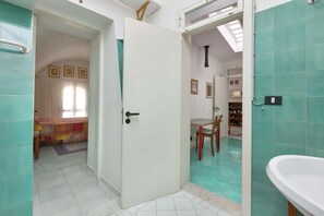 Een badkamer met een witte wastafel en een deur naar een eetruimte met een tafel en stoelen.