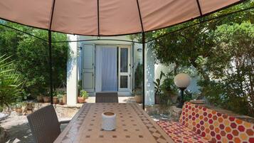 Une terrasse extérieure avec une table, des chaises et un canapé placés sous une tonnelle.