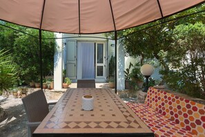 Een terras buiten met een tafel, stoelen en een bank onder een overkapping.