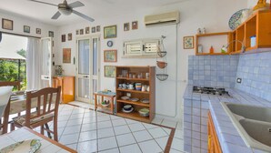 A kitchen with a tiled floor, a dining table with chairs, a ceiling fan, and a window with curtains. - Pajara Annelies (Salve)