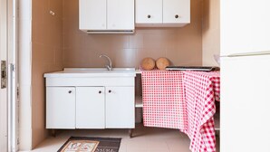 Una cocina pequeña con armarios blancos, un lavamanos y un mantel a cuadros sobre una mesita.