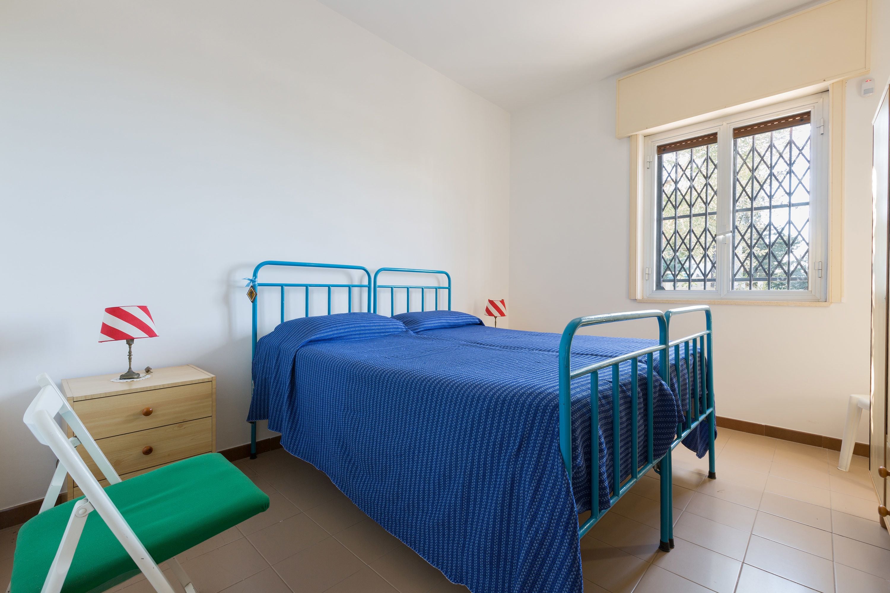 Une chambre avec un lit simple, une table de chevet, une chaise et une fenêtre donnant sur un beau paysage.