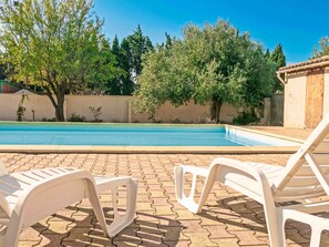 Una piscina con sillas de descanso y árboles al fondo.