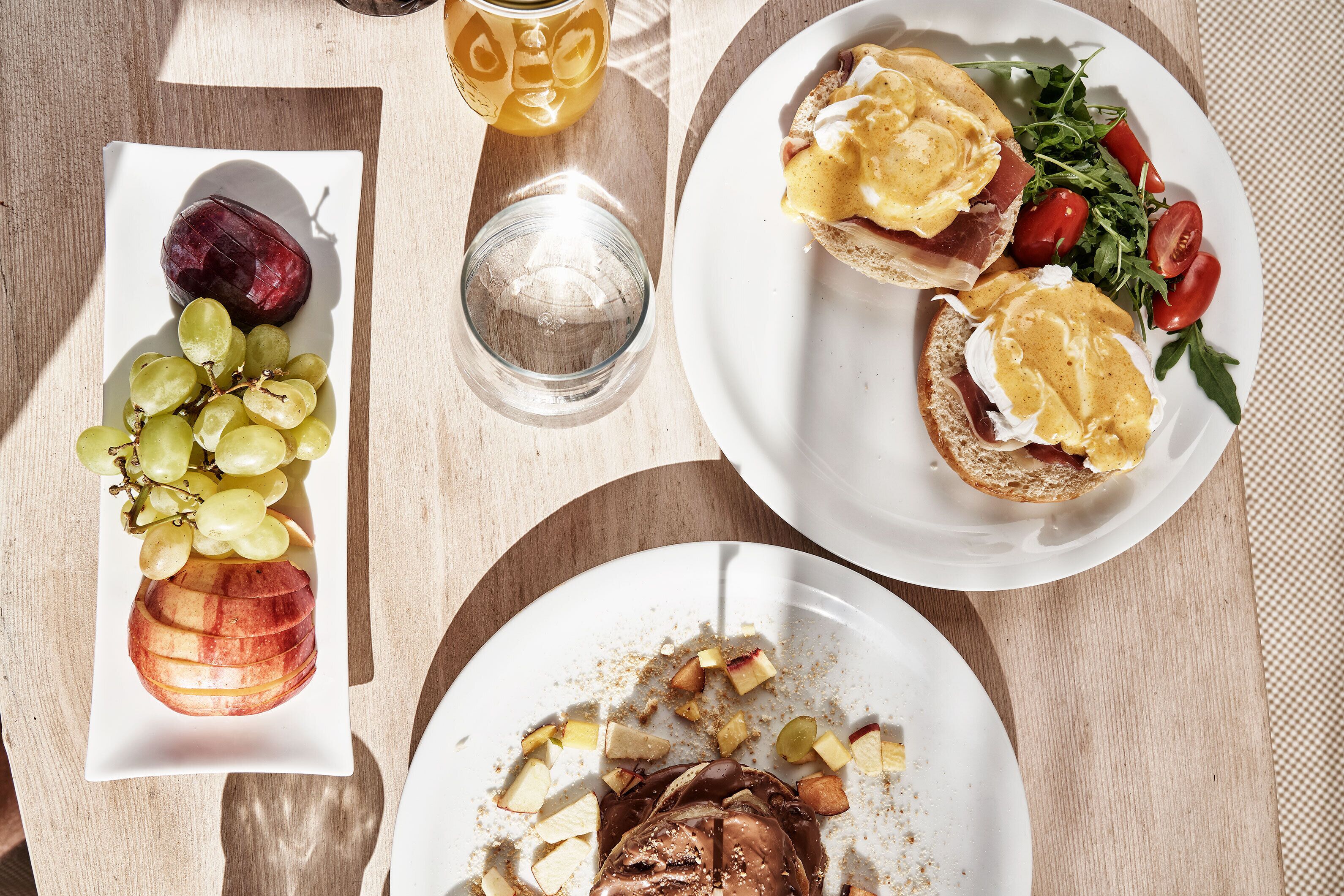 Una mesa con platos de comida, incluyendo uvas, una manzana y una ensalada con tomates cherry.