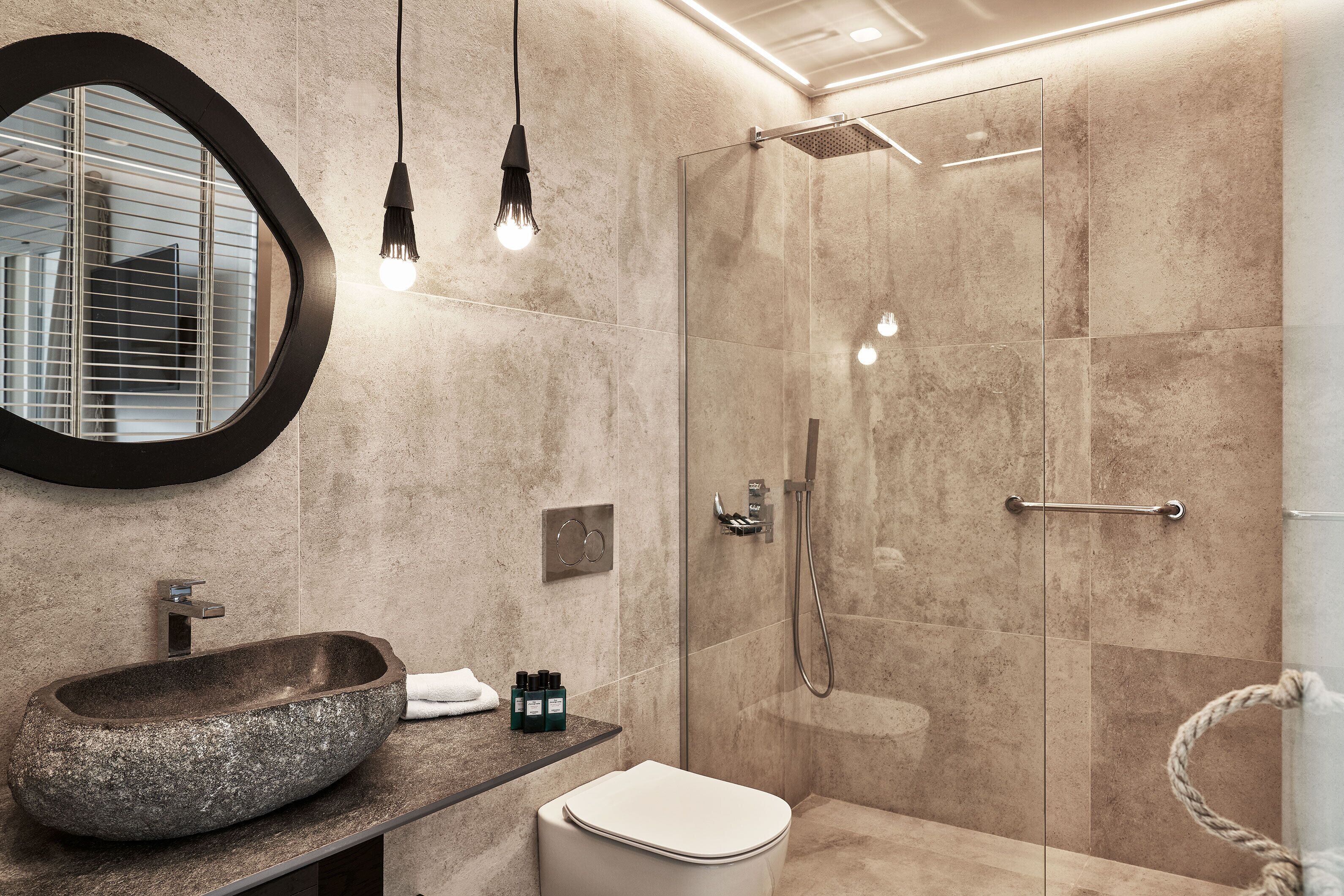 A modern bathroom with a stone sink, a toilet, and a glass shower enclosure.