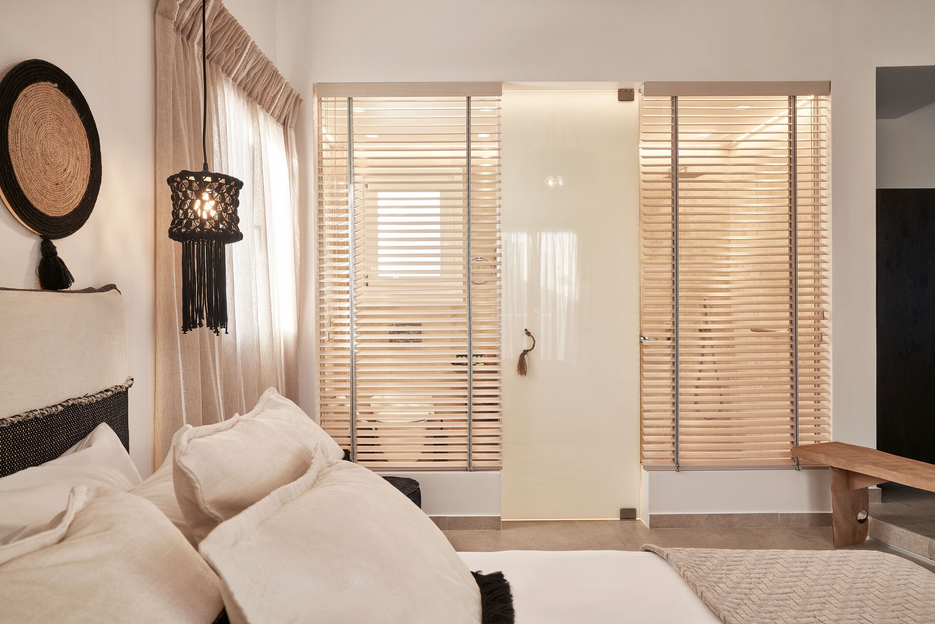 Une chambre à coucher comprenant un lit, une lampe de chevet, un miroir rond fixé au mur et une porte coulissante avec des stores en bois.
