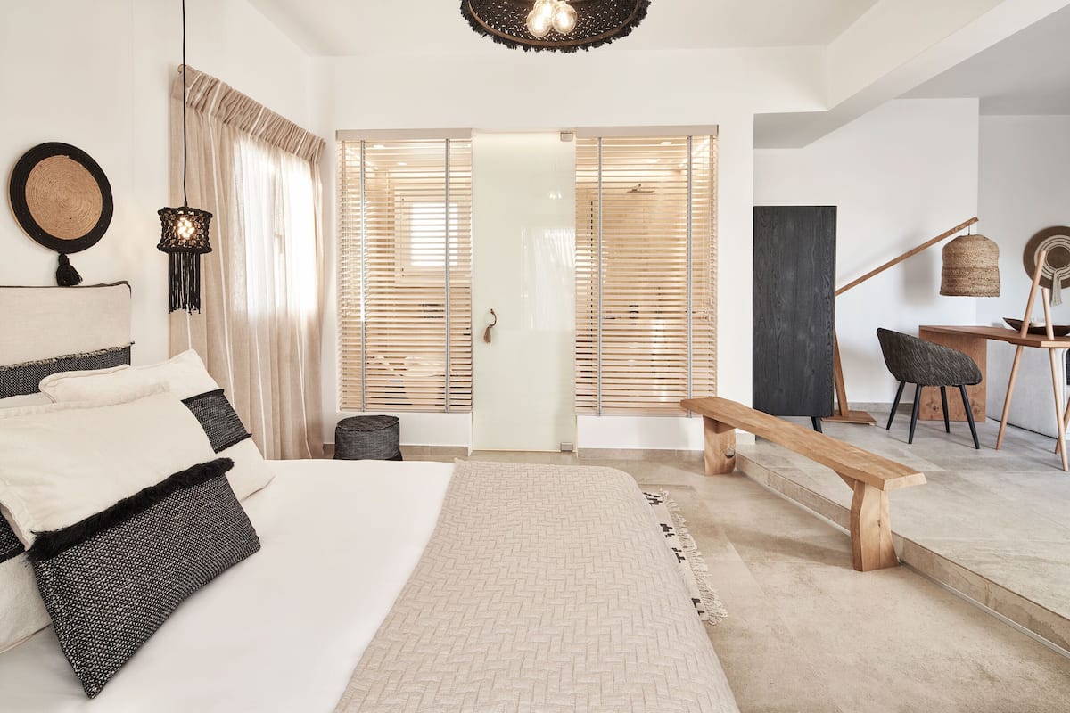 A modern bedroom with a large bed, a wooden bench, a desk, and a chair.