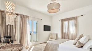 A bedroom with a bed, a chair, a television, and a view of the outdoors. - Volcano Luxury Suites Milos - Adults Only (Milos)