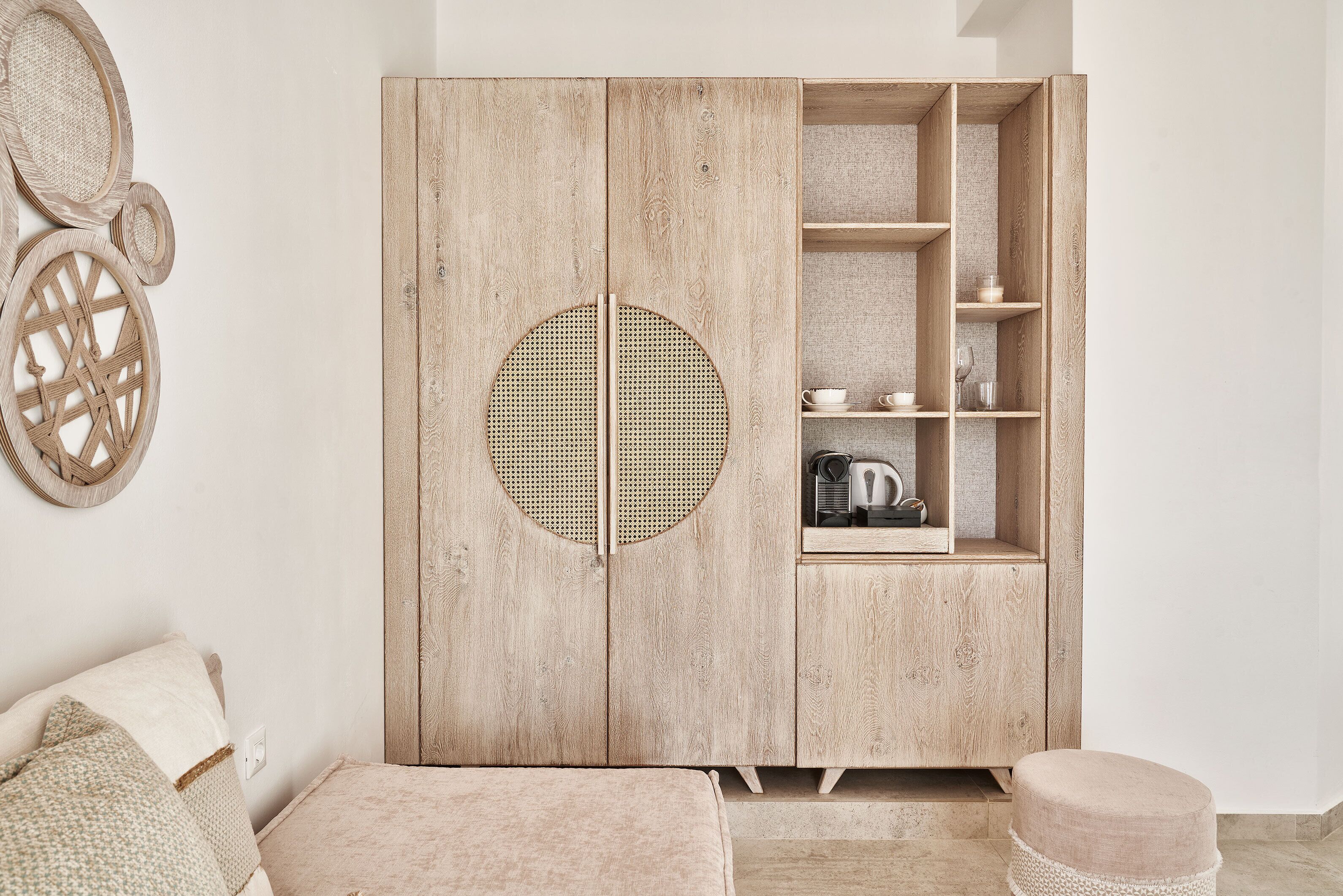 A wooden wardrobe with a circular woven door, shelves, and a small cabinet with a kettle.