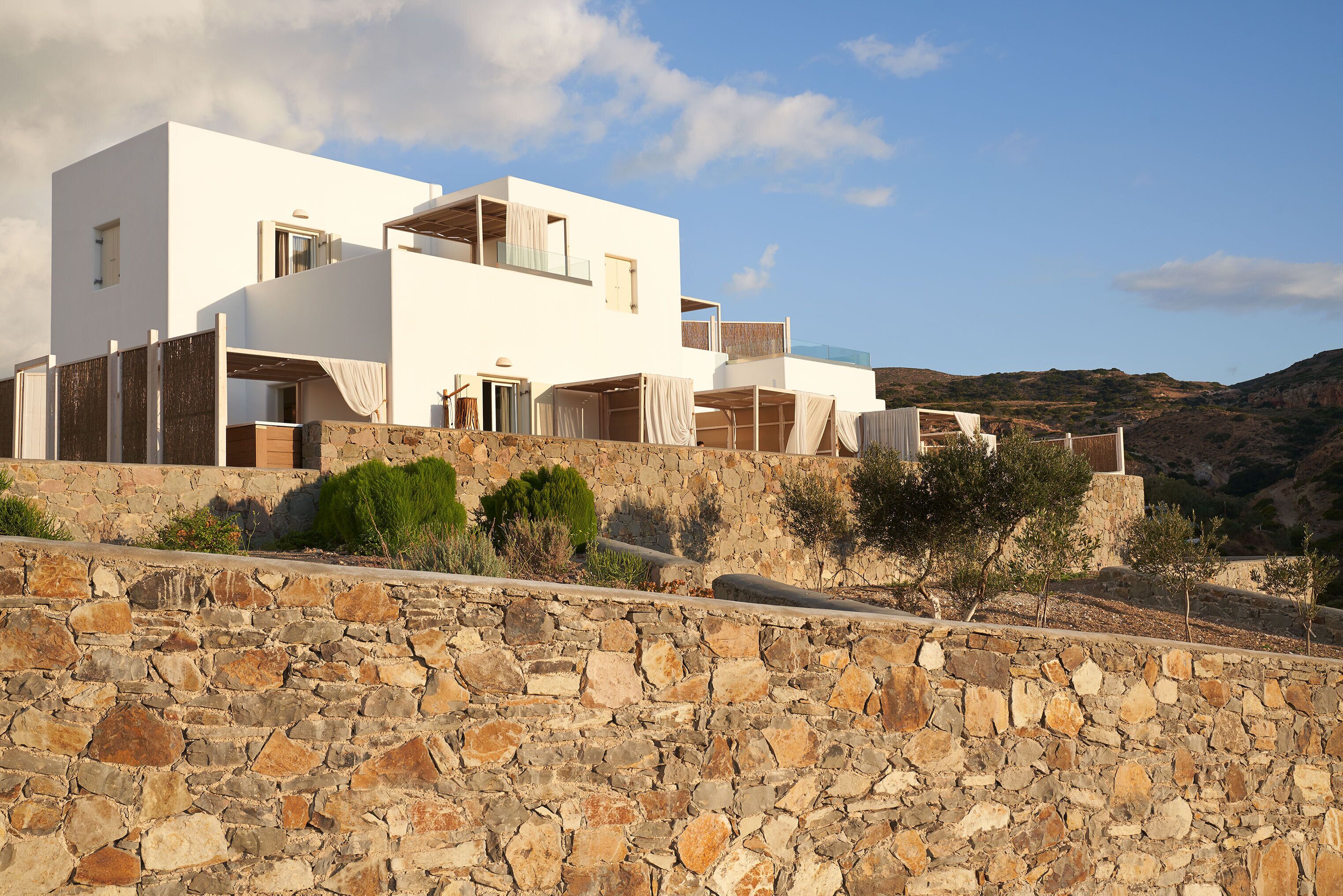 A modern white building with multiple balconies, set against a mountainous backdrop.