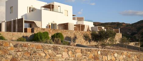 A modern white building with multiple balconies, set against a mountainous backdrop.