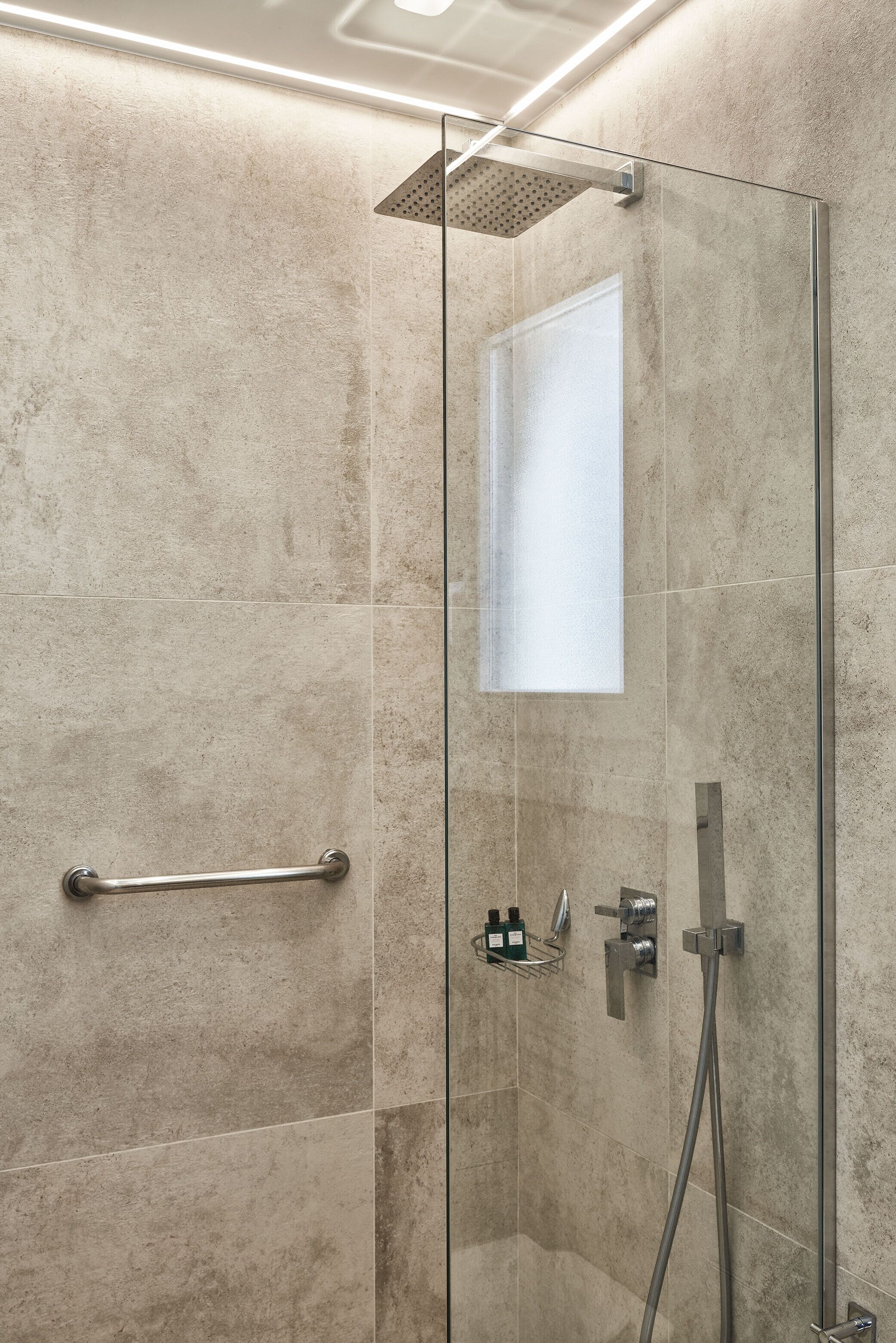 A modern shower with a glass door, a handheld showerhead, a handheld shower attachment, and a glass-enclosed window.