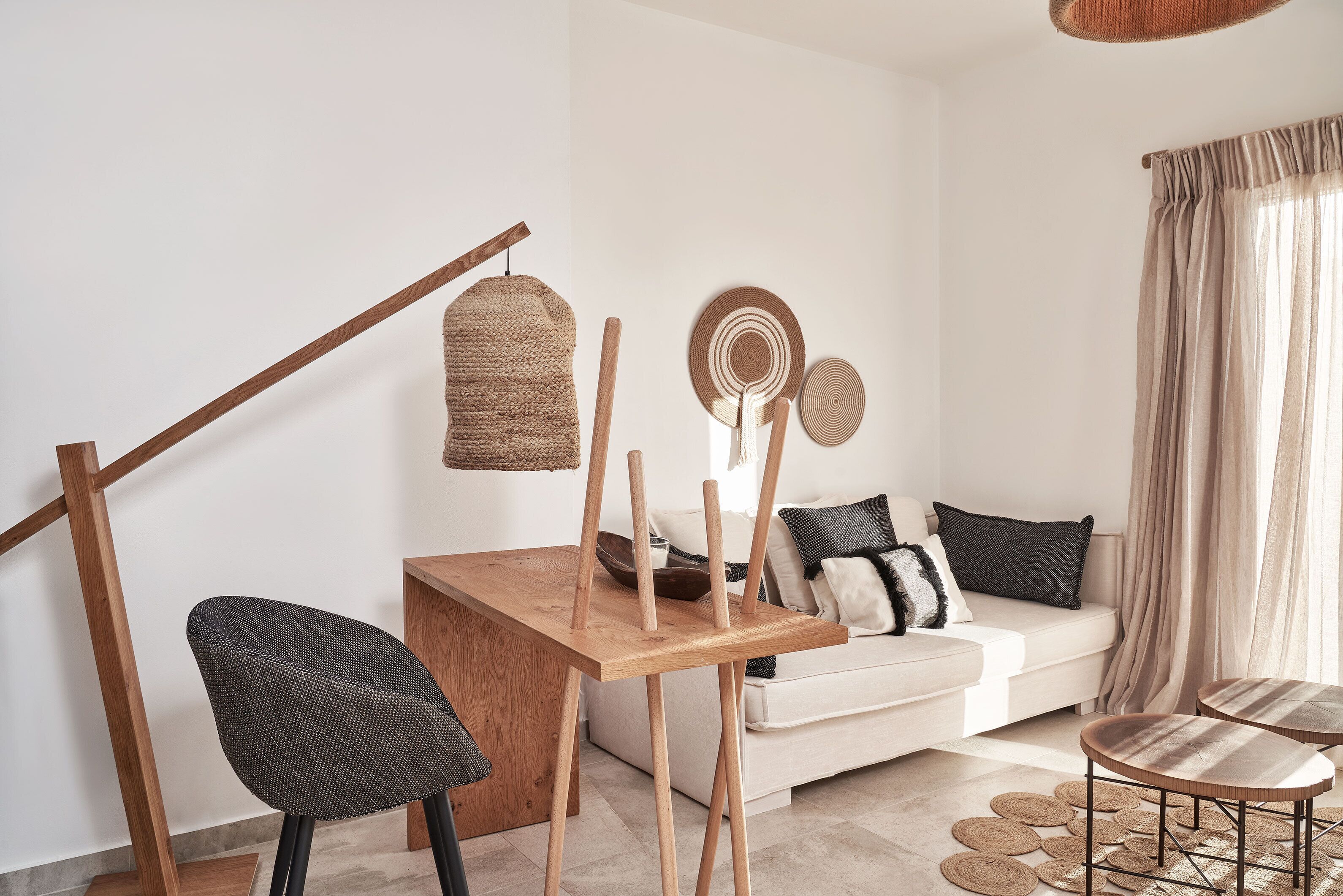 A modern living room with a wooden dining table, a black woven chair, a white sofa, and a wooden floor lamp.
