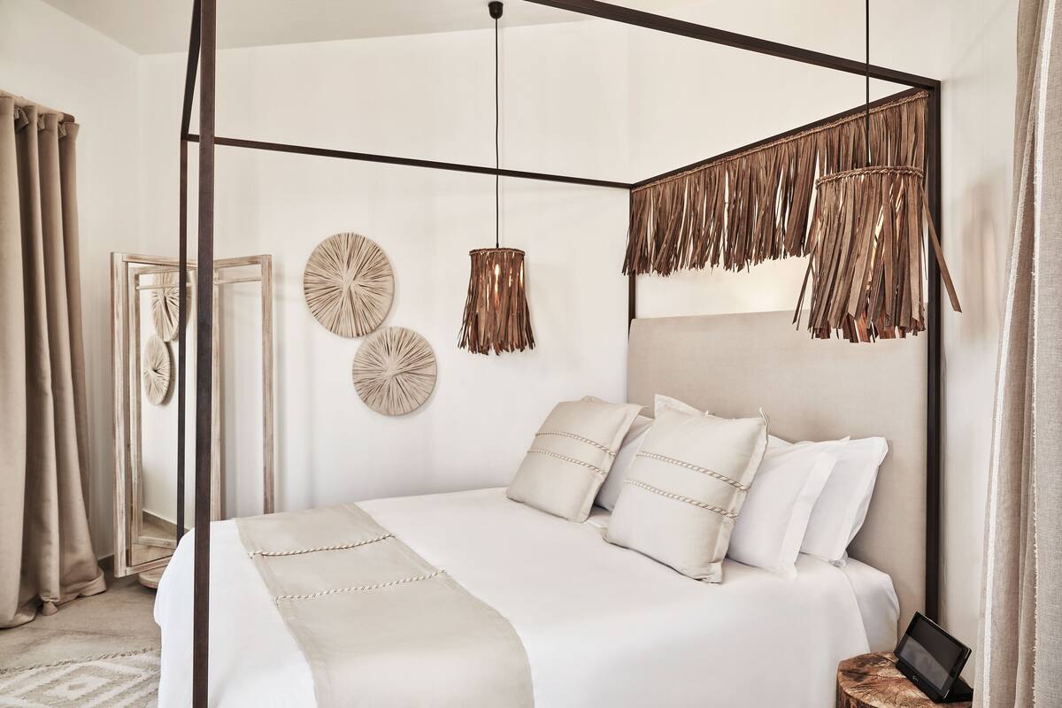 A four-poster bed with white linens and decorative pillows, a round mirror, and a wall-mounted round mirror.