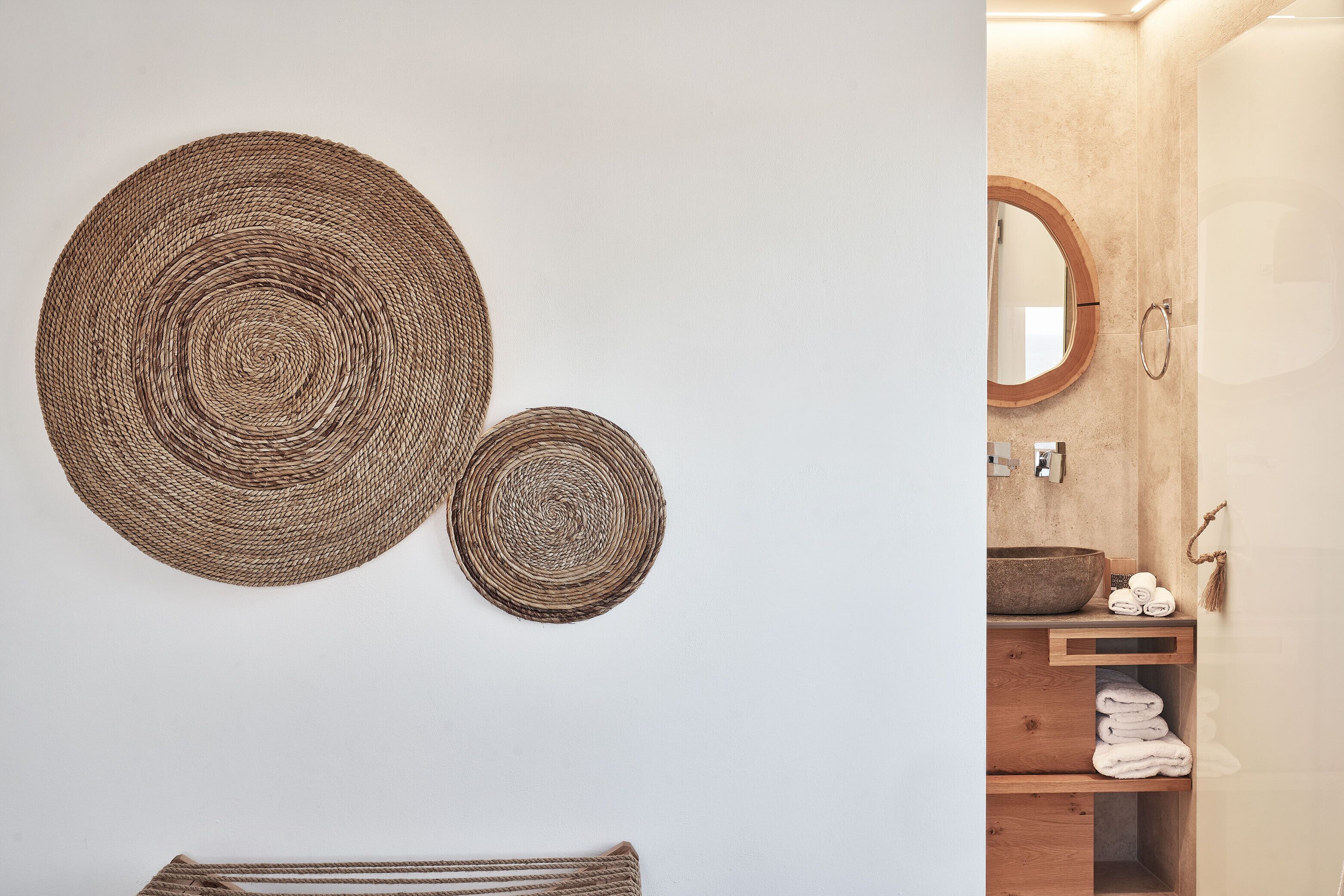 A bathroom with a wooden vanity, a round mirror, and two woven wall decorations.