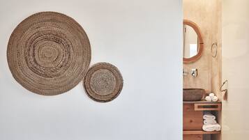A bathroom with a wooden vanity, a round mirror, and two woven wall decorations.